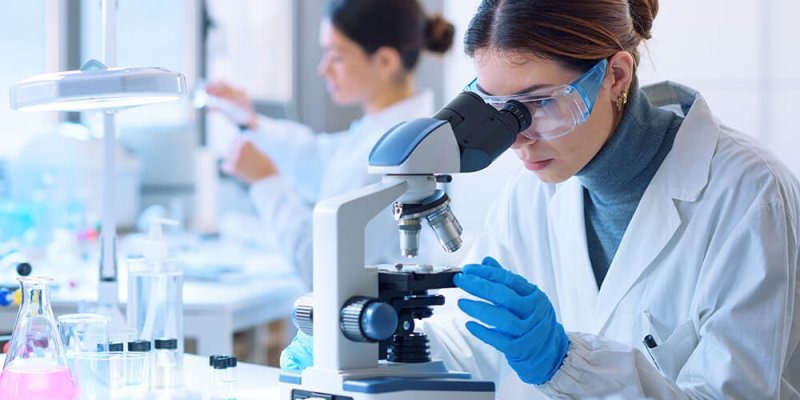 Young scientists conducting research investigations in a medical laboratory, a researcher in the foreground is using a microscope