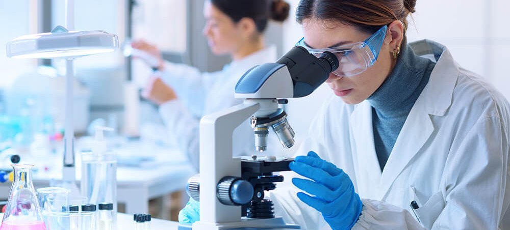 Young scientists conducting research investigations in a medical laboratory, a researcher in the foreground is using a microscope